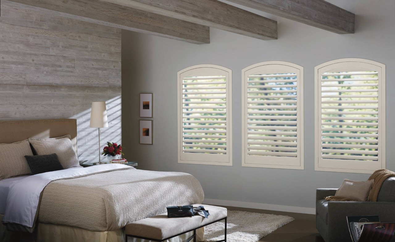 Bedroom with three windows outfitted with tan Hunter Douglas NewStyle® Hybrid Shutters near Miami, FL